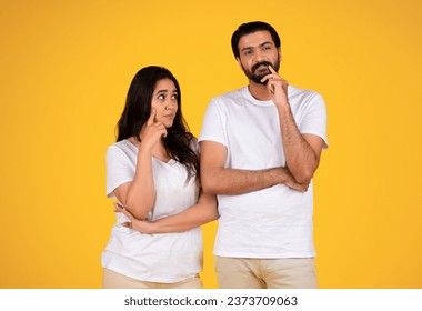Thoughtful young couple isolated on yellow studio background, both looking contemplative. Expressions serious yet calm, indicating deep thought or concern, creating somber atmosphere