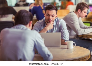 Thoughtful Young Freelancer Is Using A Laptop While Working With Other People At The Coffee Shop