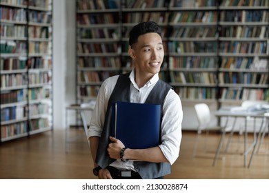 Thoughtful Young Handsome Z Generation Male Asian Student Holding Folder With Study Papers In Hands, Posing In Library, Looking In Distance Visualizing Successful Future Career, Feeling Motivated.