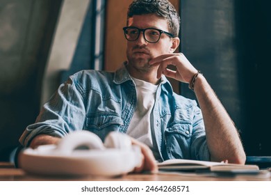 Thoughtful young hipster guy in eyewear pondering on organisation plan sitting at desktop indoors,contemplative caucasian male student spending time for learning at university campus thinking on essay - Powered by Shutterstock