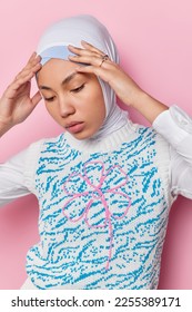 Thoughtful young Islamic woman keeps hands on head concentrated down tries to remember something wears hijab and vest has healthy skin isolated over pink background tries to gather with thoughts - Shutterstock ID 2255389171