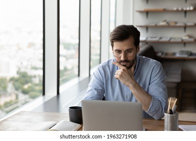 Thoughtful young male employee or worker sit at desk in office work online on laptop solve business problem. Pensive businessman use computer thinking pondering over project. Planning concept. - Shutterstock ID 1963271908