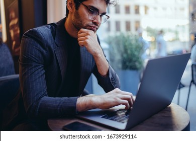 Thoughtful Young Male Entrepreneur In Eyewear For Provide Eyes Protection Watching Business Webinar Online On Modern Laptop Computer Connected To Wireless 4G Internet, Pensive Man Browsing Web Streams