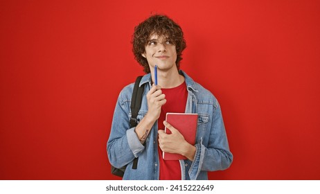 A thoughtful young man with curly hair holds a book against a red background, evoking a casual and contemplative mood. - Powered by Shutterstock