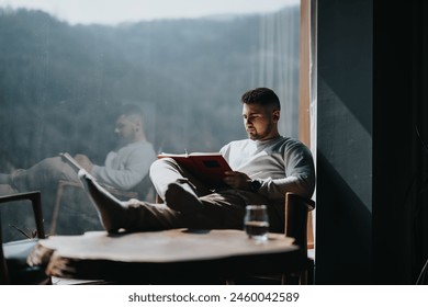 A thoughtful young man enjoys reading a book by a sunlit window, with reflections and calm vibes in a serene setting. - Powered by Shutterstock