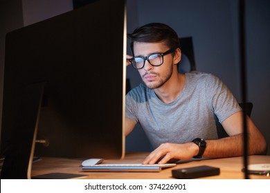 Thoughtful Young Man In Glasses Thinking And Working With Computer In Dark Room