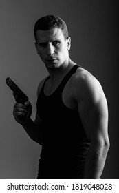 Thoughtful Young Muscular Persian Man Holding Gun And Looking Back Ready For Action In Dark Room