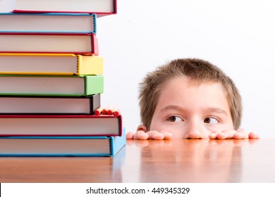 Thoughtful Young Schoolboy Eyeing Up His Books Peeping Over The Top Of His Desk At A Huge Stack Of Colorful Hardcover Textbooks