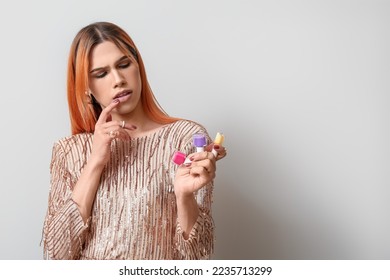 Thoughtful young transgender woman with nail polishes on light background
