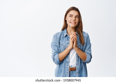 Thoughtful young woman with blond hair, squinting and staring pensive aside, steeple fingers while making up plan, thinking about something interesting, standing over white background