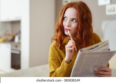 Thoughtful Young Woman Doing A Cryptic Crossword Puzzle In A Newspaper Looking Off To The Side With A Pensive Expression As She Tries To Solve A Clue