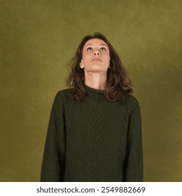 A thoughtful young woman looks upwards, against a textured olive green backdrop - Powered by Shutterstock