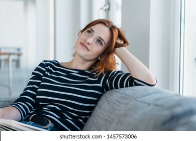 Thoughtful young woman relaxing an a sofa at home resting her head on her hand looking up with a pensive expression and quiet smile - Shutterstock ID 1457573006