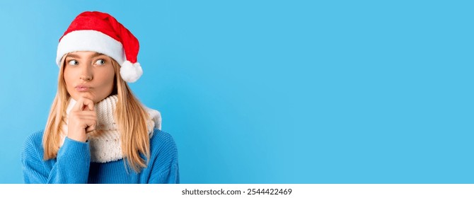 Thoughtful young woman in Santa hat, touching chin and gazing towards free space, embodying contemplation amidst the vibrant, cheerful color of blue studio backdrop - Powered by Shutterstock