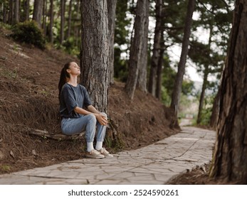 Thoughtful young woman sitting on a stone path in a serene forest, enjoying nature and reflecting in a peaceful atmosphere under tall trees - Powered by Shutterstock