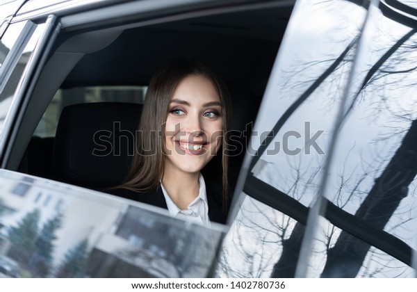 Thoughtful young woman in a suit\
sitting in the backseat of a car and looking through the\
window