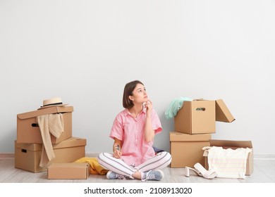 Thoughtful young woman with wardrobe boxes and things near light wall