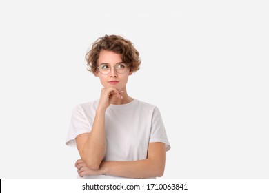 Thoughtful young woman in a white shirt and eyeglasses looking at the copy space in a right upper corner isloated over white background. Concept of thinking