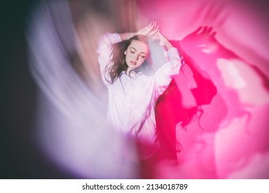 Thoughtfulness, insight. A young beautiful girl in euphoria is standing with closed eyes illuminated by a beam of light. Studio portrait in crimson lighting. - Shutterstock ID 2134018789