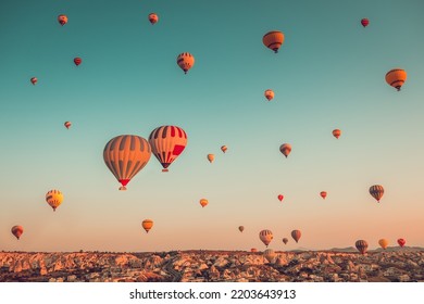 Thousands of colorful hot air balloons flight above mountains - Cappadocia panorama, sunrise view. Goreme valley wide landscape. Vintage retro orange blue toning filter. Tourism, travel, holidays - Shutterstock ID 2203643913