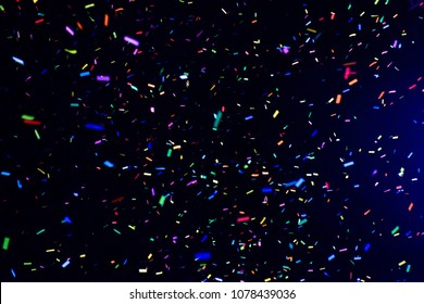 Thousands of confetti fired on air during a festival at night. Image ideal for backgrounds. Multicolor are the confetti in the picture. The sky as background is black. Cold tonality