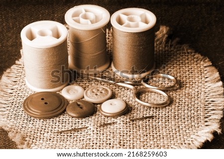 THREAD ON REELS, BUTTONS, SCISSORS AND DARNING NEEDLE ON HESSIAN IN SEPIA