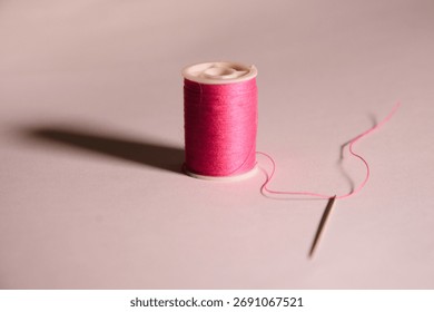 Thread spool with pink thread and threaded needle on white background