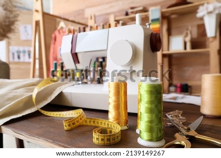 Thread spools with measuring tape and tailor's scissors on table in atelier, closeup