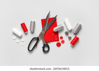 Thread spools with scissors, buttons, fabric and thimble on grey background