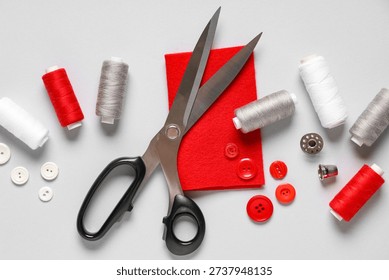 Thread spools with scissors, buttons, fabric and thimble on grey background