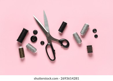 Thread spools with scissors and buttons on pink background