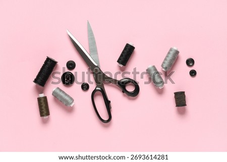 Thread spools with scissors and buttons on pink background