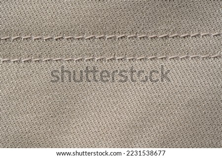 Thread stitching on light denim. Beige jeans fabric background or denim texture. Close up view