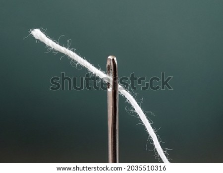 Thread white is threaded through eye of needle, close-up macro view