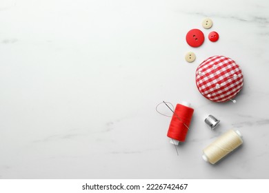 Threads and other sewing supplies on white marble table, flat lay. Space for text