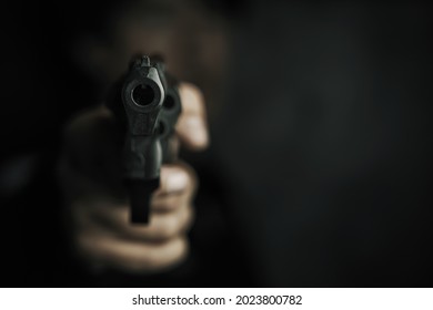 Threat of firearms. Muzzle of gun in man's hand is pointed at camera. Male criminal holds revolver on black background. Attack or defense.