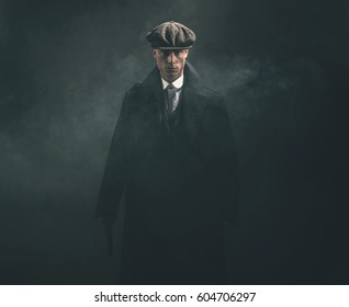 Threatening retro 1920s english gangster holding gun in smoky room.