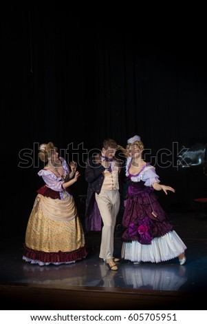 Three actors play roles on stage, a young man in an old coat and two female actresses in medieval dresses with wide skirts
