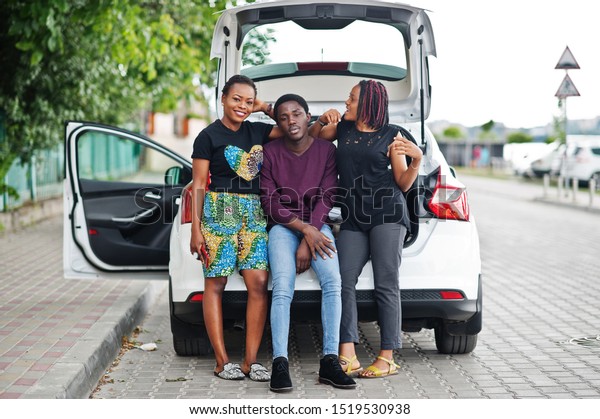Three african american friends sit in the trunk of\
the car.