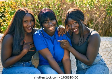 Three african american friends smiling happy sitting on the bench at the park.