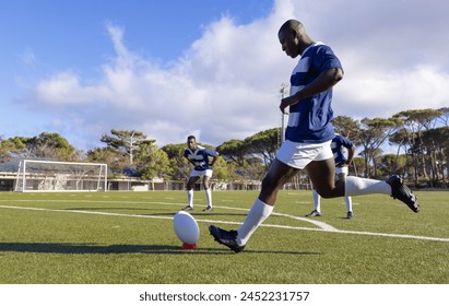 Three African American young male athletes training with a rugby ball on a field outdoors. Wearing sporty blue outfits, they show strong and fit physiques, focusing on the game. - Powered by Shutterstock