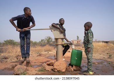 Three African Children Filling Up Water In A Plastic Tank At A Borehole Pump In A Rural Community In Sub-Saharan Africa. Child Labor Concept.