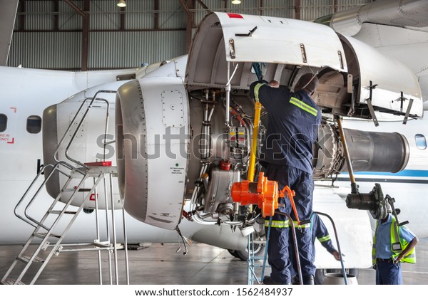 Three African mechanics repairing a plane engine\
in the hangar
