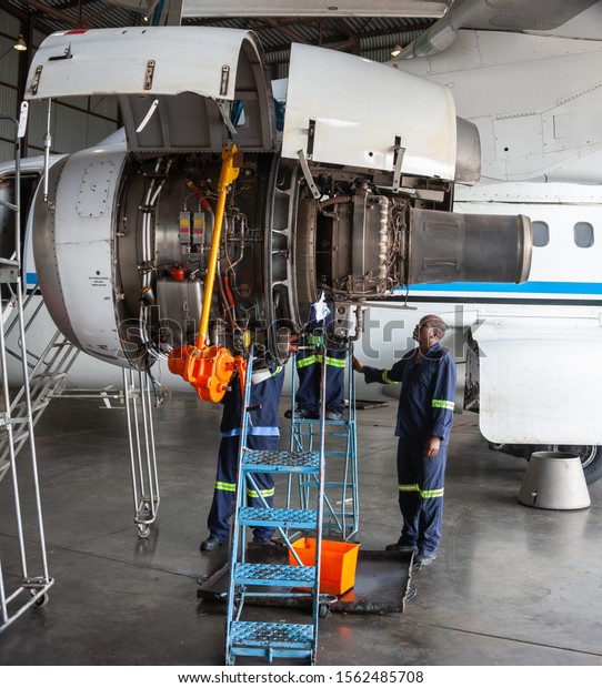 Three African mechanics repairing a plane engine\
in the hangar