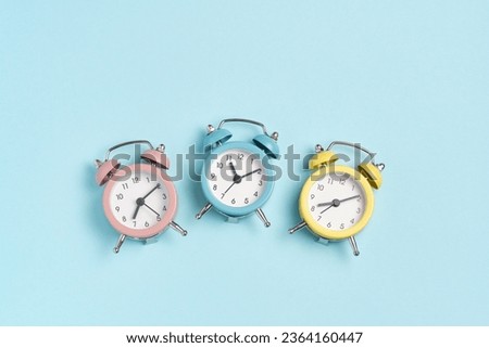 Three alarm clocks of different colors show different times. Start of the day, waking up, morning, different time zones.
