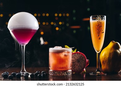 Three Alcoholic Cocktails, Purple, Orange And Yellow Colors On The Table. Variety Of Colorful Alcoholic Drinks 