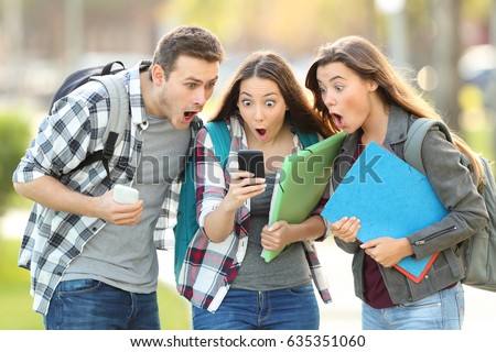 Three amazed students checking on line content on a smart phone in the street