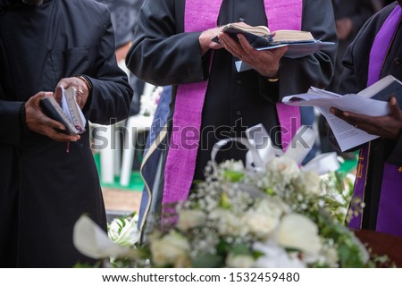 Three Anglican priests attending a funeral, next to the grave