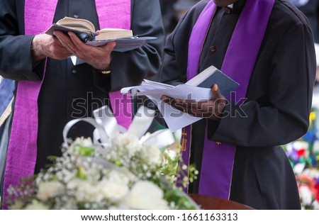 Three Anglican priests attending a funeral, next to the grave