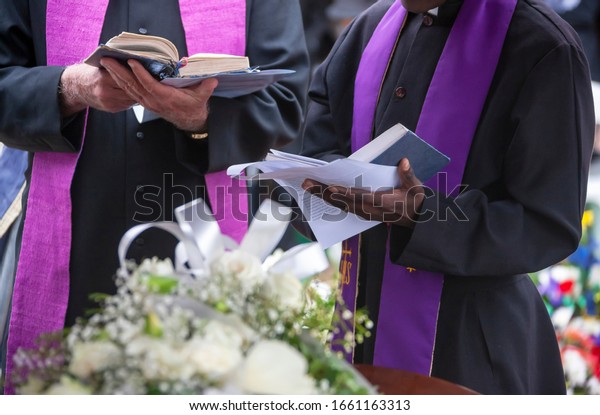 Three Anglican priests attending a funeral, next to\
the grave